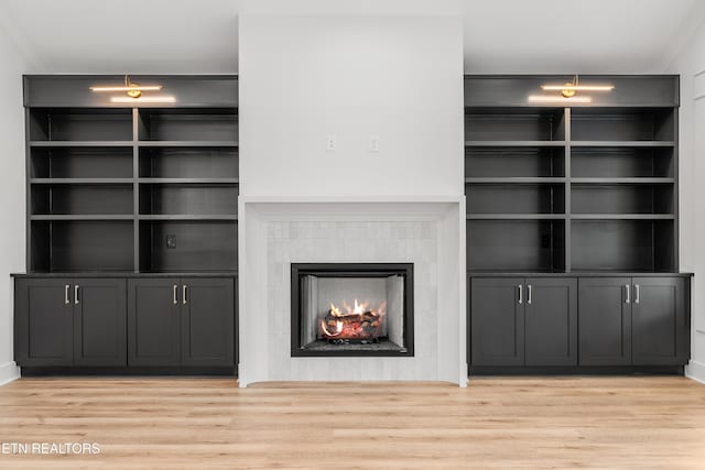 unfurnished living room featuring light wood-type flooring, built in shelves, and a tiled fireplace