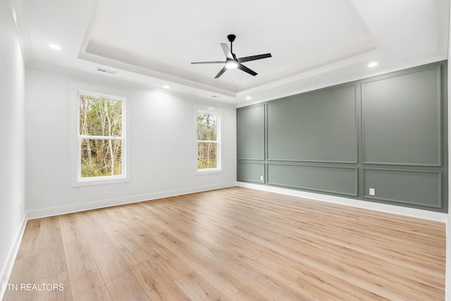 spare room with a decorative wall, light wood-type flooring, ceiling fan, and a tray ceiling