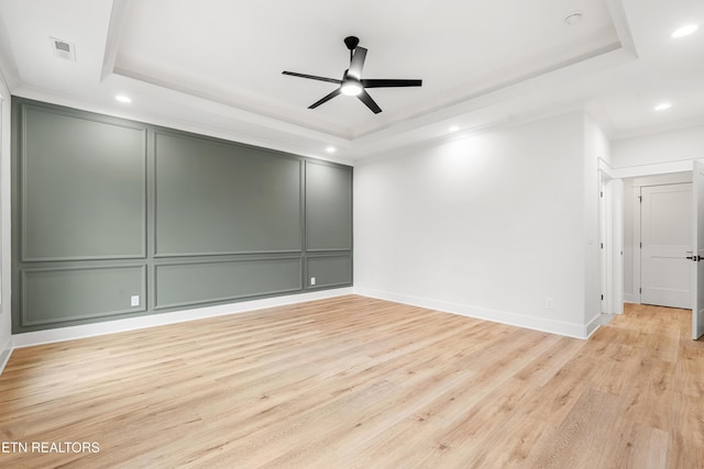 spare room featuring light wood-style floors, crown molding, a decorative wall, and a tray ceiling