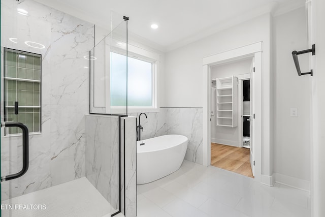 bathroom featuring a soaking tub, a marble finish shower, a walk in closet, crown molding, and tile walls