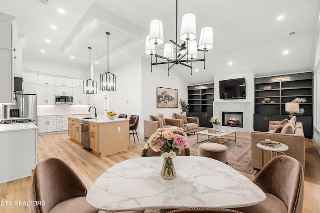 dining area featuring a chandelier, recessed lighting, light wood-style floors, a warm lit fireplace, and lofted ceiling with beams