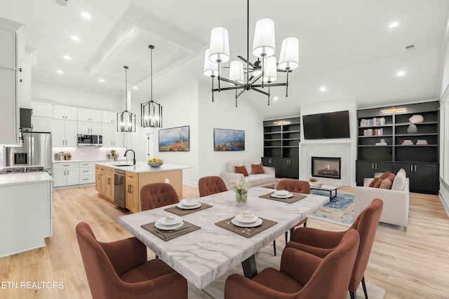 dining room with a towering ceiling, light wood-style flooring, recessed lighting, a glass covered fireplace, and a notable chandelier