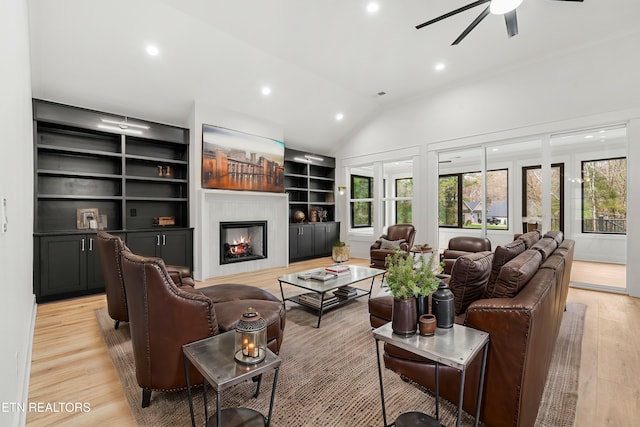 living room with light wood-type flooring, vaulted ceiling, a warm lit fireplace, recessed lighting, and a ceiling fan