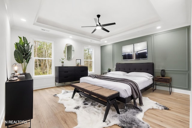 bedroom with multiple windows, light wood-style floors, and a tray ceiling