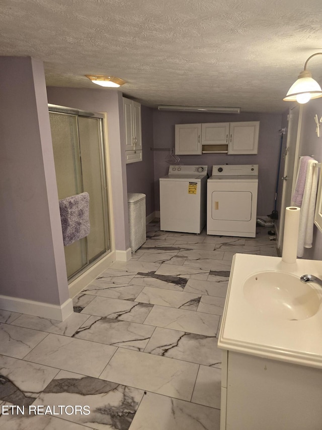 bathroom with independent washer and dryer, vanity, a shower with shower door, and a textured ceiling