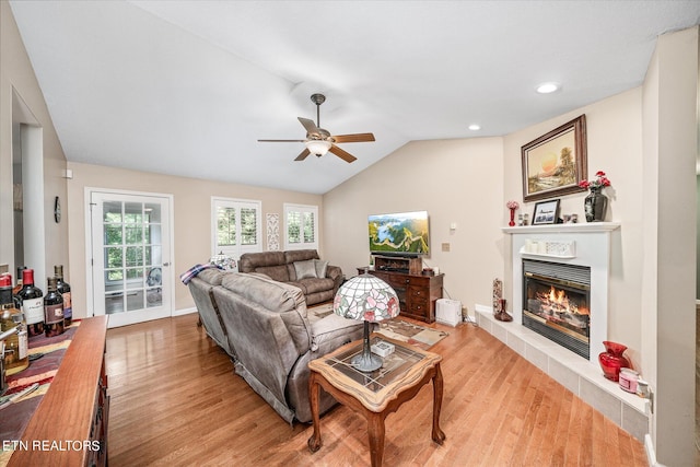 living room featuring ceiling fan, light hardwood / wood-style flooring, vaulted ceiling, and a tiled fireplace