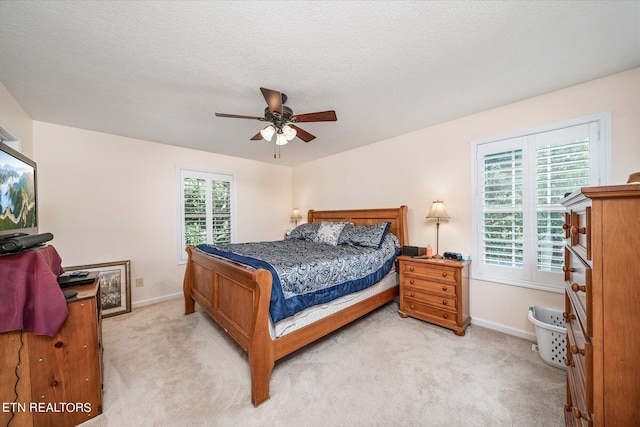 bedroom featuring light carpet, ceiling fan, a textured ceiling, and baseboards