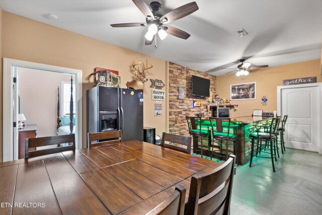 dining room with bar area, concrete floors, and ceiling fan