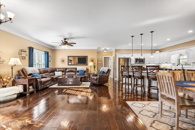 living room featuring dark wood-type flooring, ceiling fan with notable chandelier, and crown molding