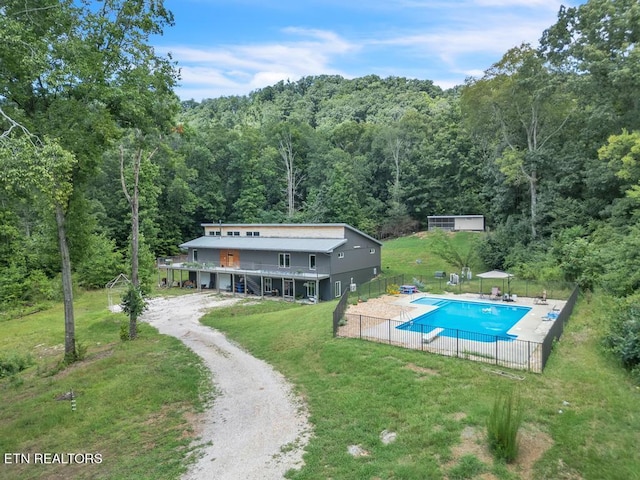 view of swimming pool featuring a patio area, a fenced in pool, a view of trees, fence, and a yard