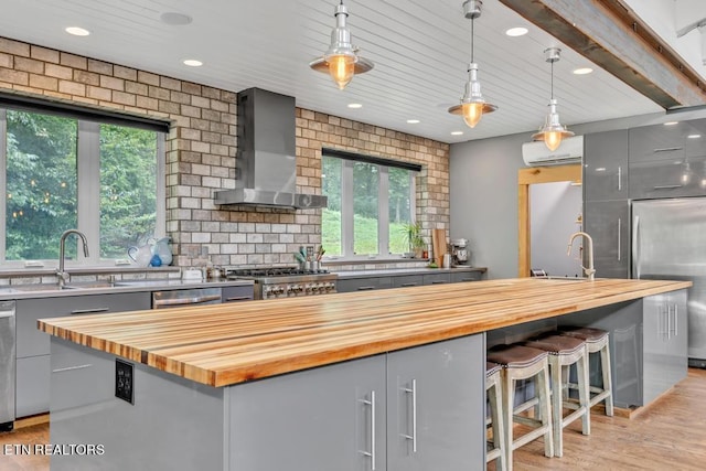 kitchen featuring gray cabinets, hanging light fixtures, a center island, butcher block counters, and wall chimney exhaust hood