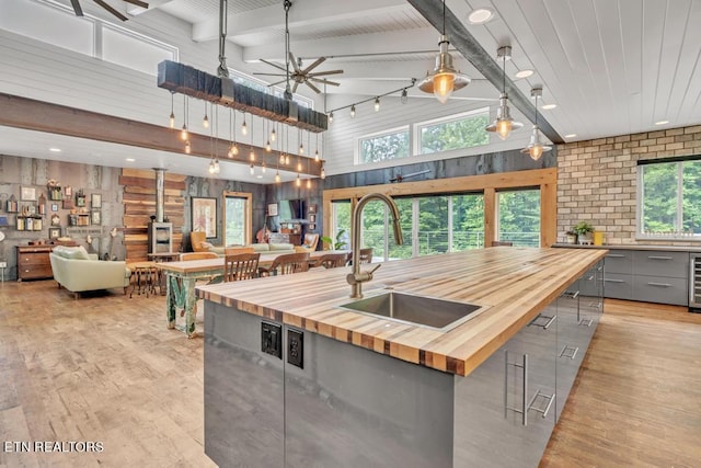 kitchen featuring wooden counters, hanging light fixtures, an island with sink, ceiling fan, and rail lighting