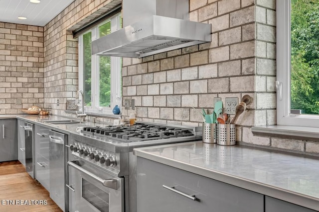 kitchen featuring sink, light hardwood / wood-style flooring, gray cabinets, range hood, and high end stainless steel range