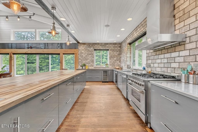 kitchen featuring wooden counters, gray cabinetry, hanging light fixtures, stainless steel appliances, and wall chimney exhaust hood