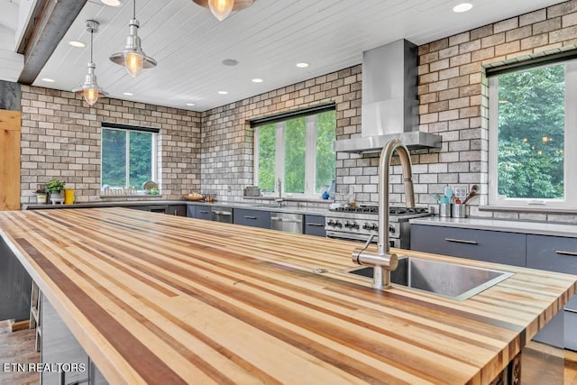 kitchen with wall chimney exhaust hood, high end stove, decorative light fixtures, backsplash, and butcher block counters