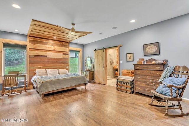 bedroom featuring ensuite bath, light wood-type flooring, a barn door, and ceiling fan