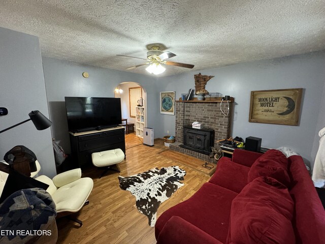 living room with ceiling fan, a fireplace, light hardwood / wood-style flooring, and a textured ceiling