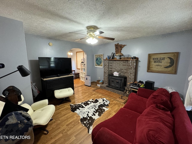 living room with hardwood / wood-style flooring, a textured ceiling, ceiling fan, and a wood stove