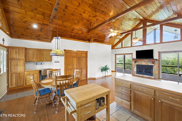 kitchen with ceiling fan, wooden ceiling, a stone fireplace, hanging light fixtures, and high vaulted ceiling