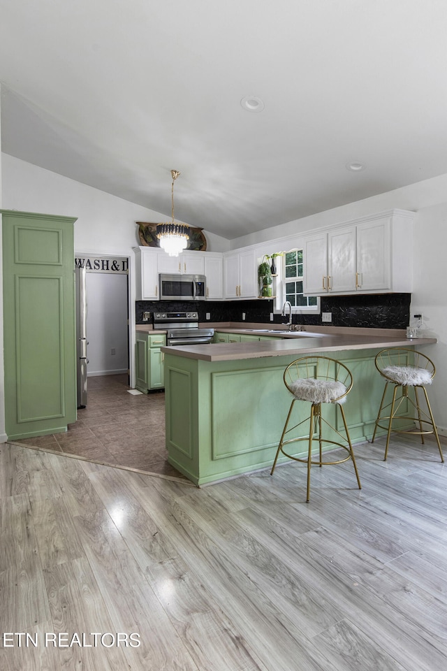 kitchen featuring stainless steel appliances, white cabinetry, light wood-type flooring, lofted ceiling, and green cabinetry