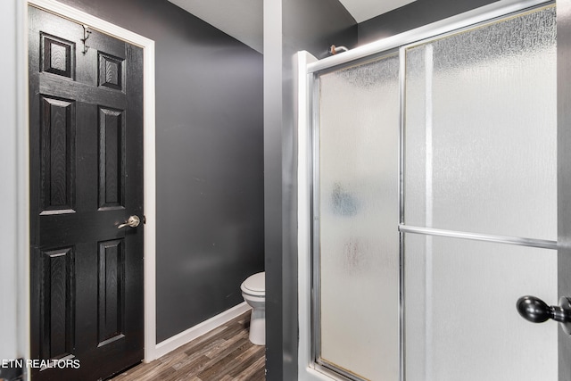 bathroom with hardwood / wood-style flooring, a shower with shower door, and toilet