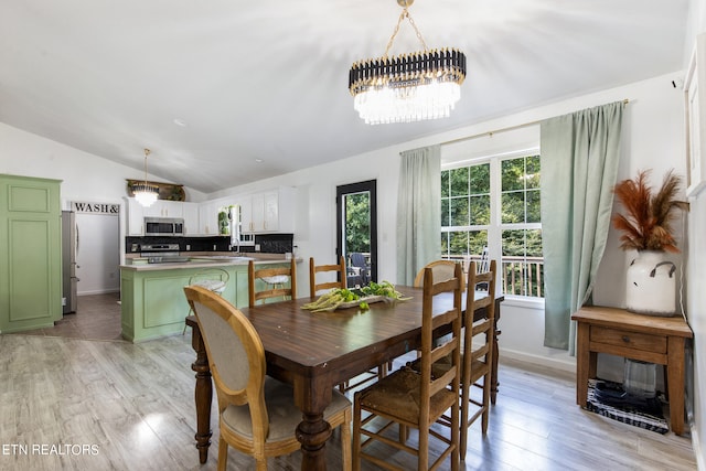 dining room featuring a notable chandelier, vaulted ceiling, and light wood-type flooring