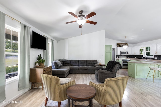 living room with sink, light wood-type flooring, vaulted ceiling, and plenty of natural light