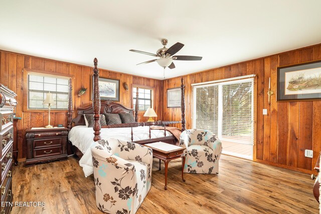 bedroom featuring multiple windows, ceiling fan, wood walls, and wood-type flooring