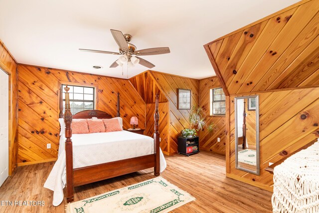 bedroom with ceiling fan, wood walls, and light hardwood / wood-style floors