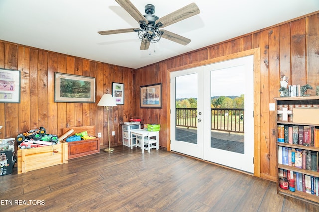 sitting room with wood finished floors, a ceiling fan, wood walls, and french doors