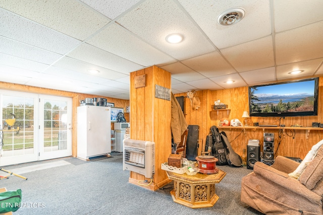 living room with a drop ceiling, carpet floors, and wooden walls