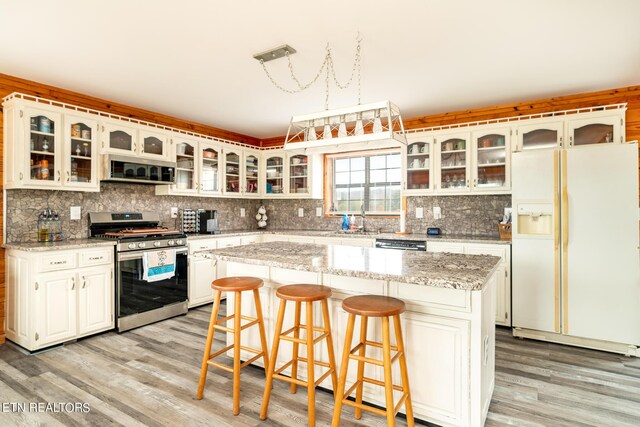 kitchen featuring decorative backsplash, white fridge with ice dispenser, gas stove, and a kitchen island