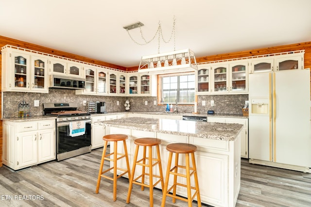 kitchen with stainless steel range with gas cooktop, tasteful backsplash, white fridge with ice dispenser, and light wood-style flooring