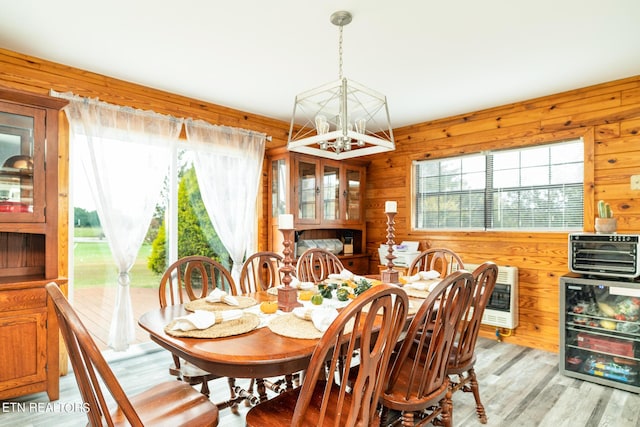 dining room featuring light wood-style flooring, a notable chandelier, heating unit, wood walls, and beverage cooler