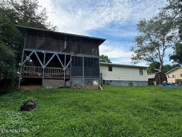 rear view of house featuring a lawn, a sunroom, a deck, and a storage shed