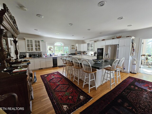 kitchen with white cabinets, a large island, glass insert cabinets, a kitchen breakfast bar, and backsplash