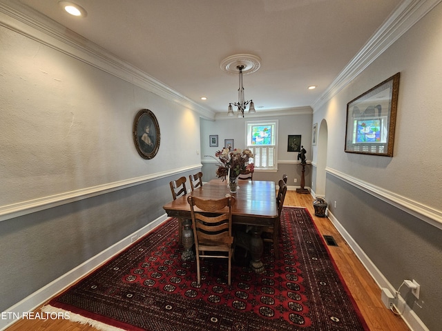 dining room with arched walkways, visible vents, ornamental molding, wood finished floors, and baseboards