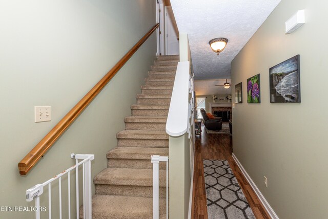 stairs featuring ceiling fan, hardwood / wood-style flooring, a textured ceiling, and a brick fireplace