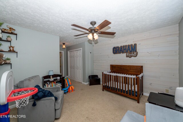 carpeted bedroom featuring a textured ceiling, a nursery area, a closet, and ceiling fan