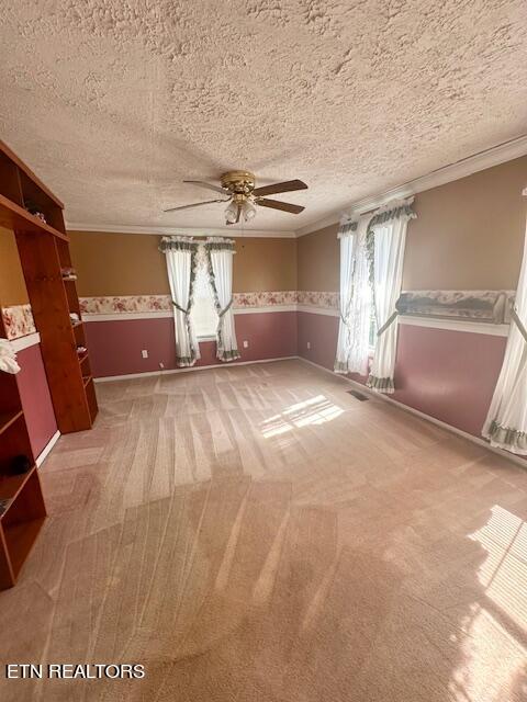 carpeted empty room featuring ceiling fan, ornamental molding, and a textured ceiling