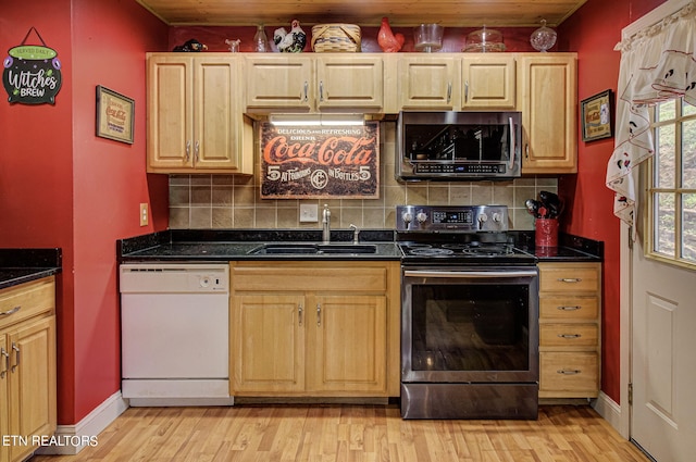 kitchen featuring tasteful backsplash, sink, light wood-type flooring, stainless steel appliances, and dark stone countertops