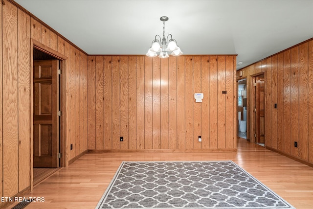 interior space featuring light hardwood / wood-style flooring, wooden walls, and an inviting chandelier