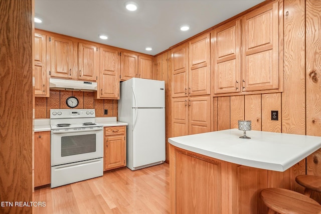 kitchen with wooden walls, light wood-type flooring, a kitchen breakfast bar, and white appliances