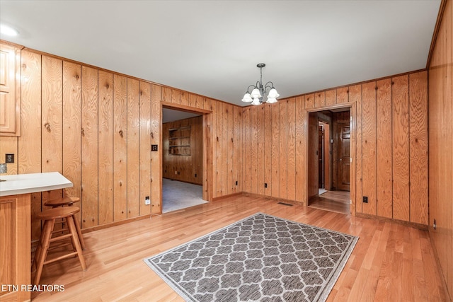 dining area with wood walls, a chandelier, and light hardwood / wood-style floors