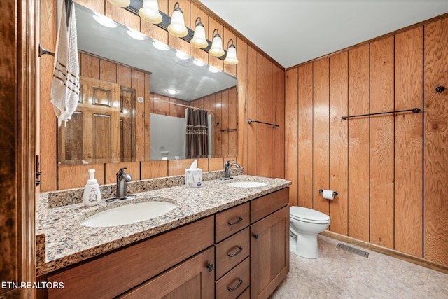 bathroom featuring dual vanity, wooden walls, and toilet