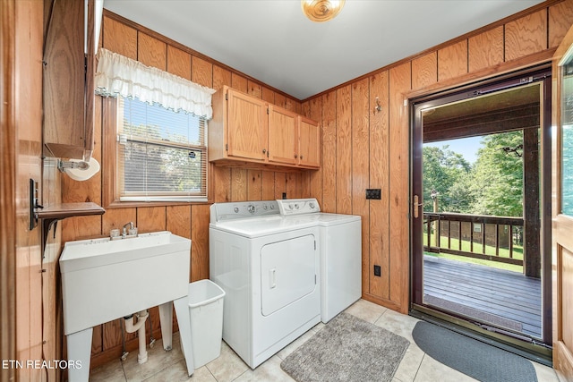 clothes washing area with washing machine and dryer, wood walls, plenty of natural light, and cabinets