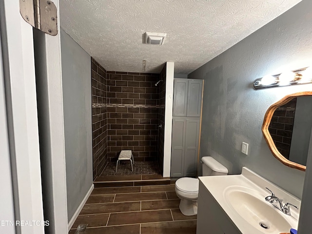 bathroom with a textured ceiling, toilet, tile patterned floors, vanity, and tiled shower