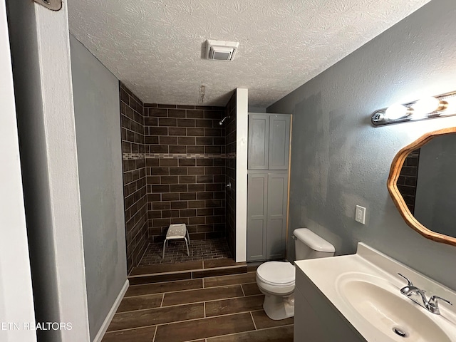 bathroom featuring a textured ceiling, tiled shower, toilet, and vanity