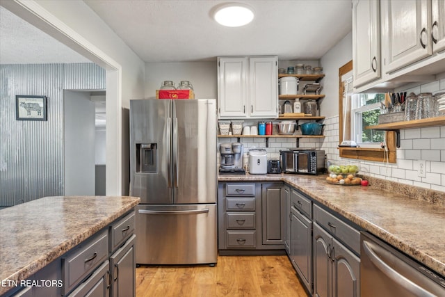 kitchen with gray cabinets, tasteful backsplash, appliances with stainless steel finishes, and light hardwood / wood-style floors