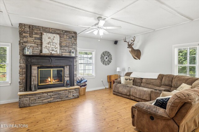 living room featuring ceiling fan, light wood-type flooring, and a stone fireplace